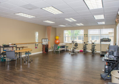 Large open gym area with treatment table, cardio equipment, and manual therapy desk